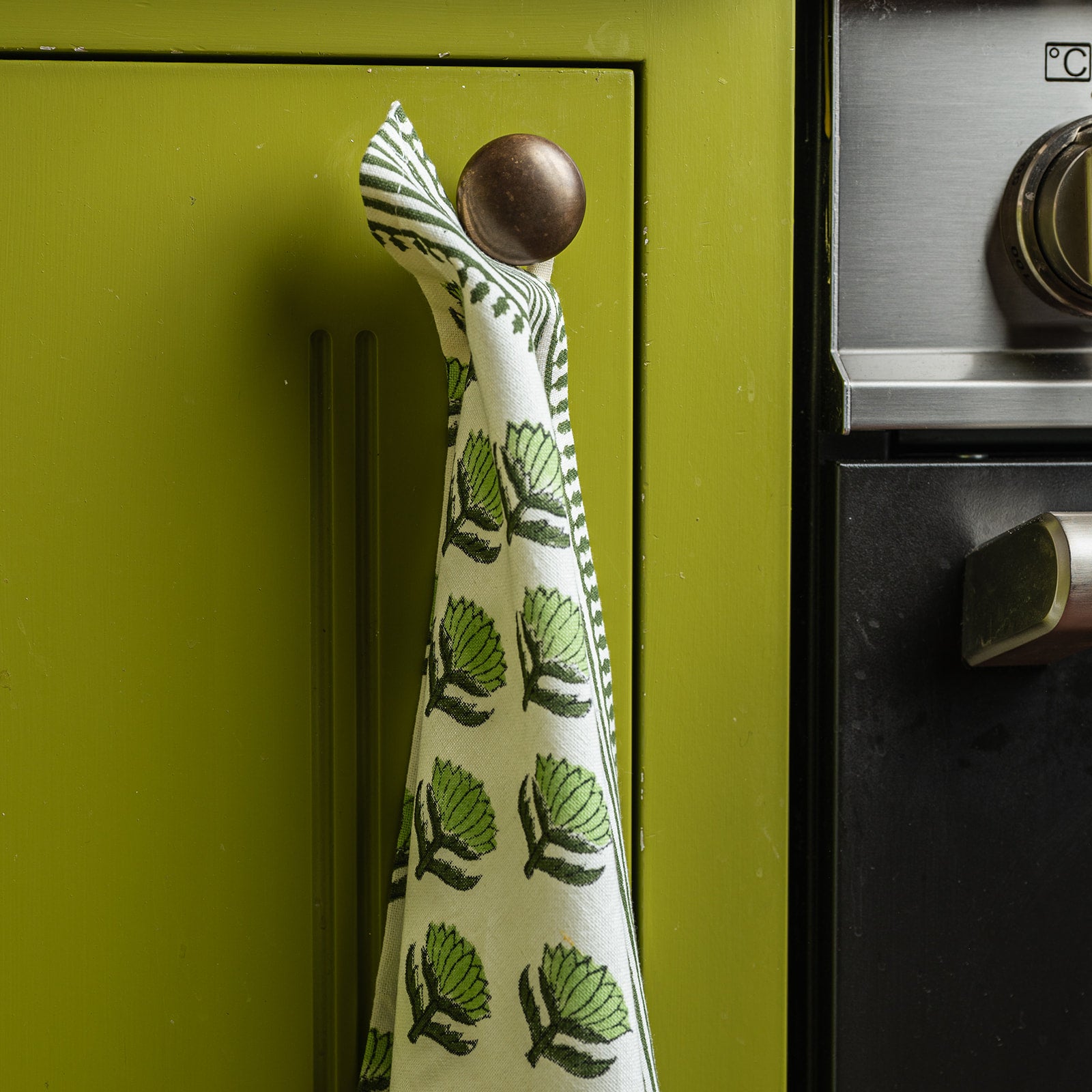 Tea towel with green leaf pattern hanging on a green cabinet handle