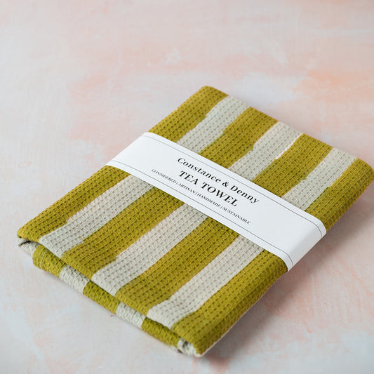 Folded green and white striped tea towel with a label on a soft pink background
