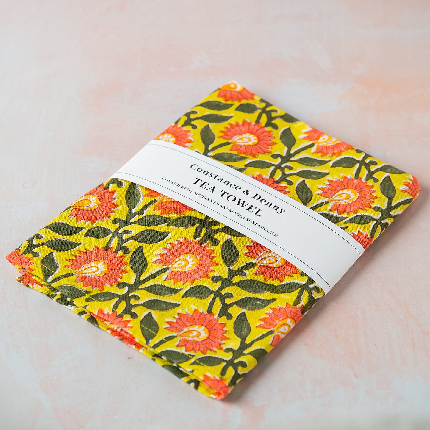 Floral patterned tea towel with a label on a light pink background