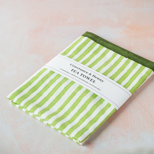Green and white striped tea towel with a label on a light pink background