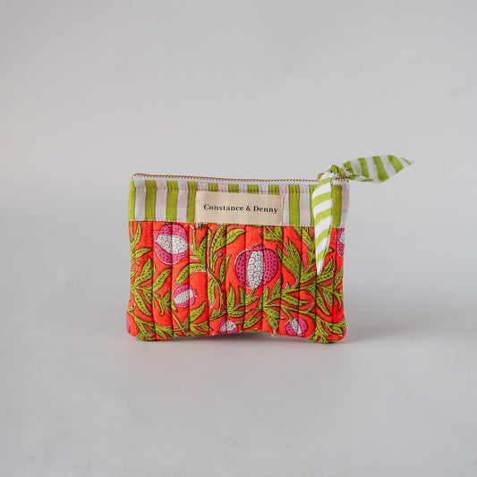 A small fabric zip pouch by Constance & Deny, featuring a vibrant pink and green floral print on the front, a green and white striped top border, and a matching striped ribbon zipper pull, set against a plain light gray background.