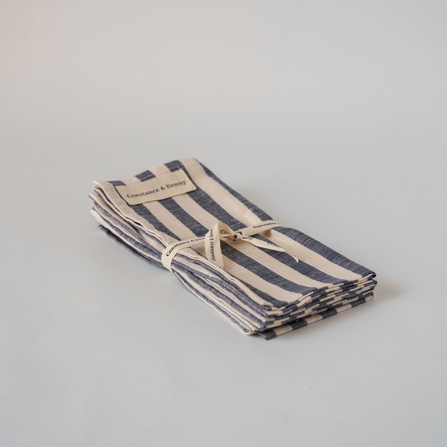A folded striped linen napkin with navy blue and cream horizontal stripes, tied with a matching ribbon and a small paper label that reads 'Constance & Henry'.