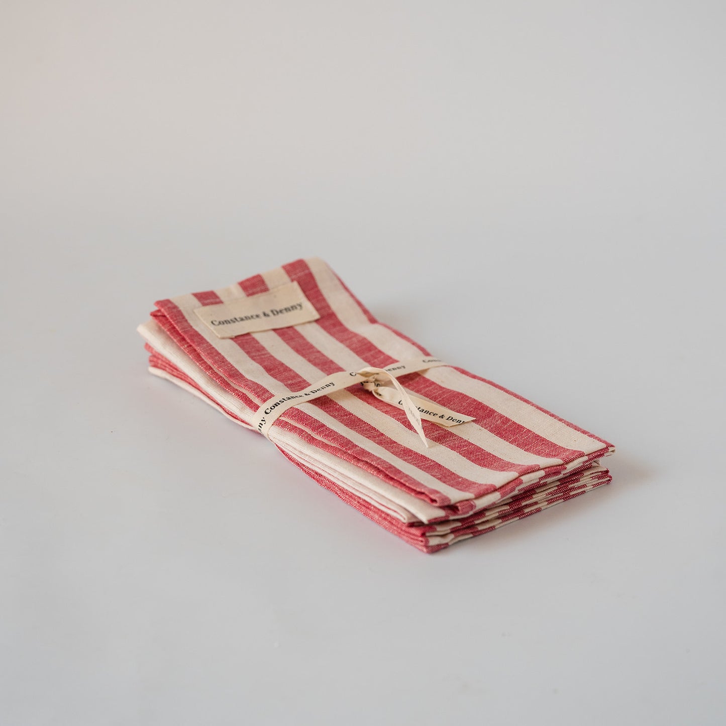 A stack of folded striped kitchen towels or napkins in red and cream, tied with a string and labeled 'Candlelight & Scenery', on a light gray background.