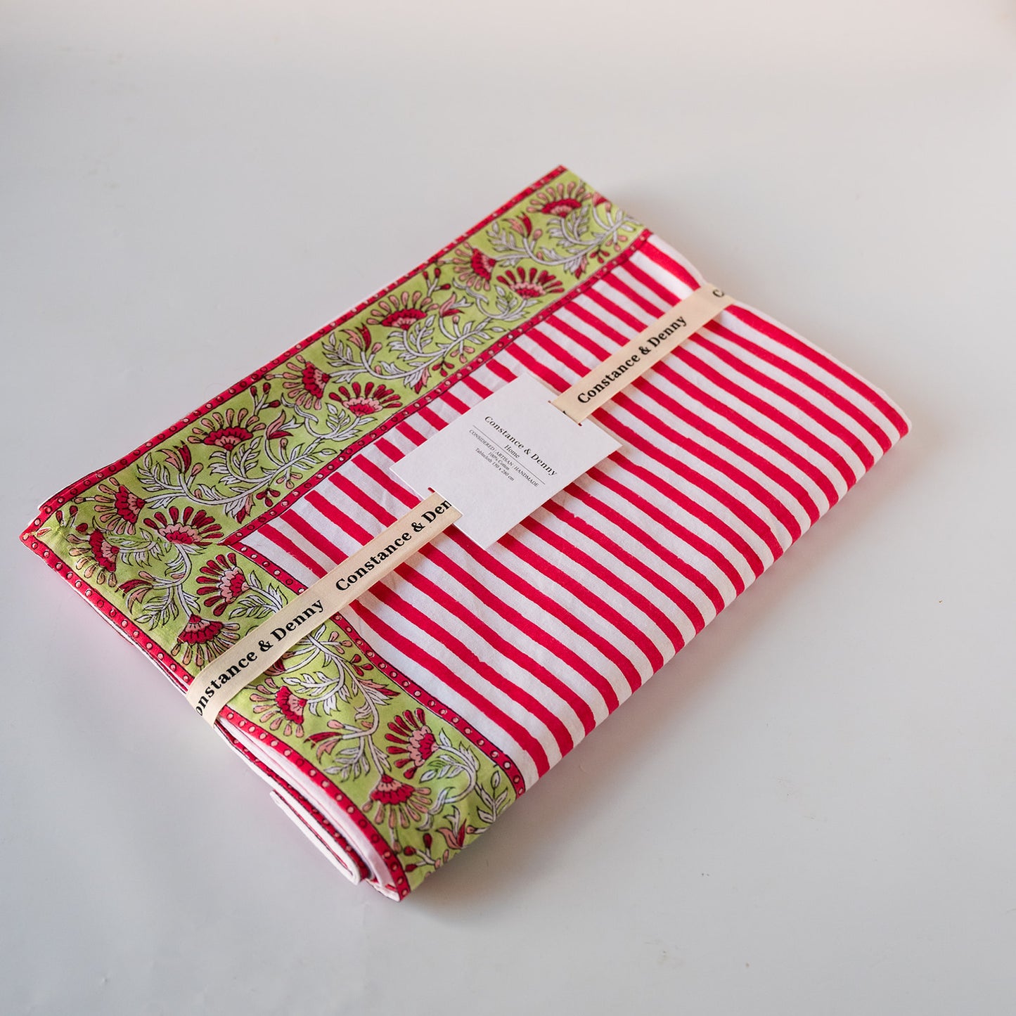 A folded fabric bundle with red and white stripes on one side and a green, red, and white floral border on the other, wrapped with a paper band labeled 'Constance & Dilly'.