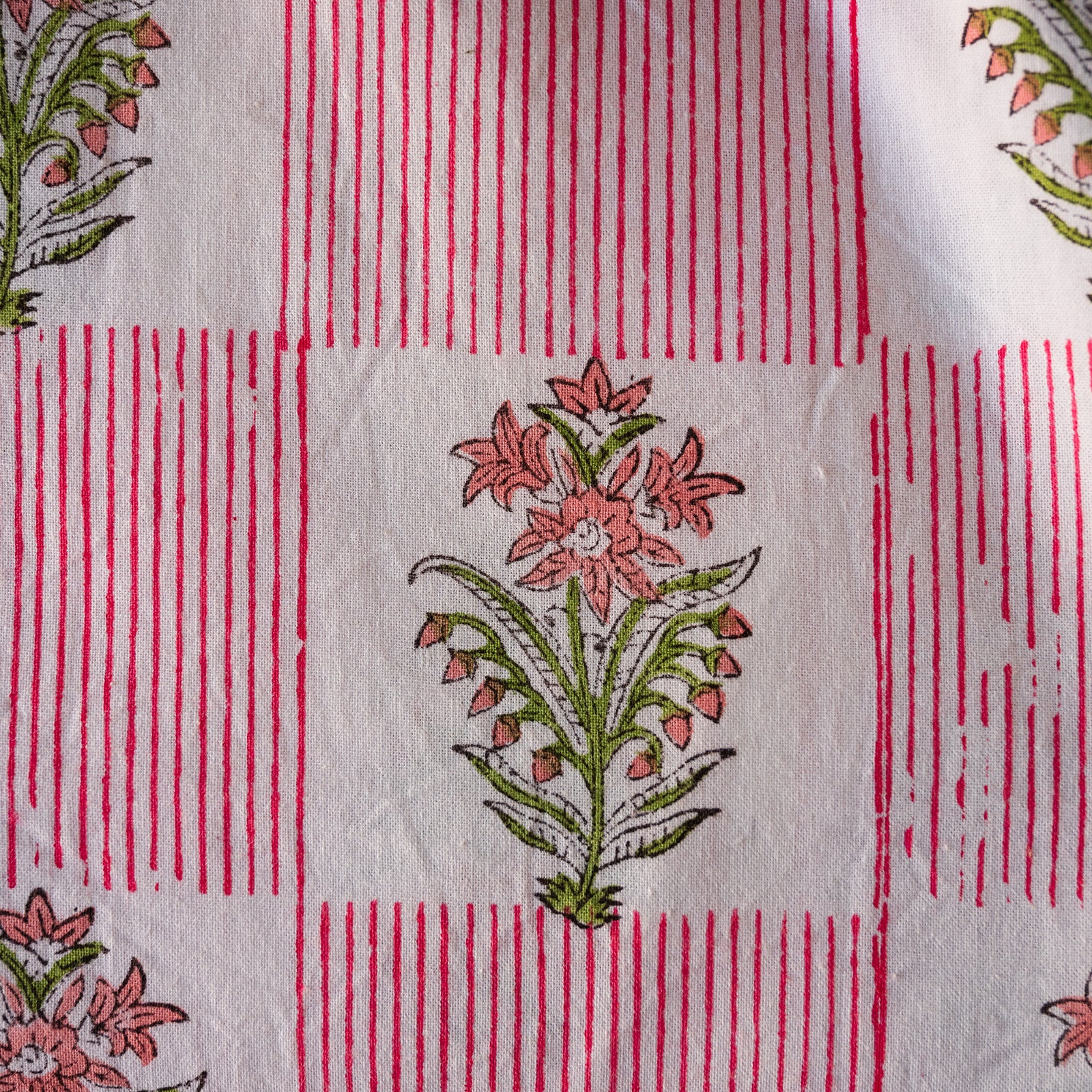A close-up of a white fabric with a red and green block-printed pattern of flowers and vertical red stripes.