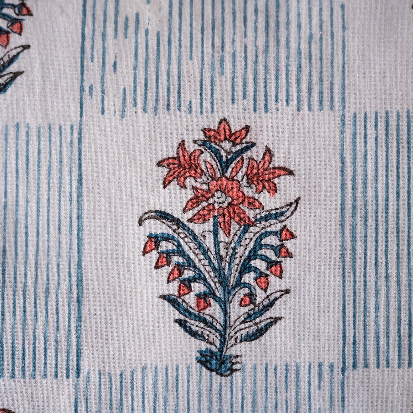 A close-up of a white fabric with a blue vertical stripe pattern and a central coral-red and blue floral block print.