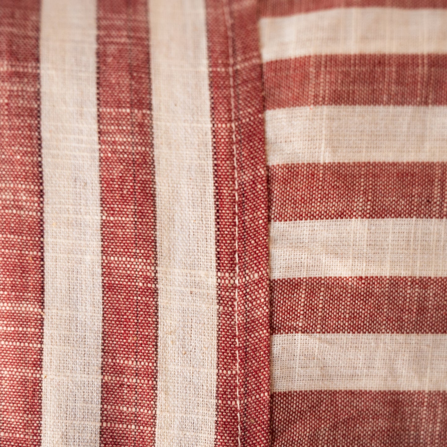 Close-up of a woven textile with alternating vertical red stripes and horizontal off-white stripes, showing the fabric texture and stitching.