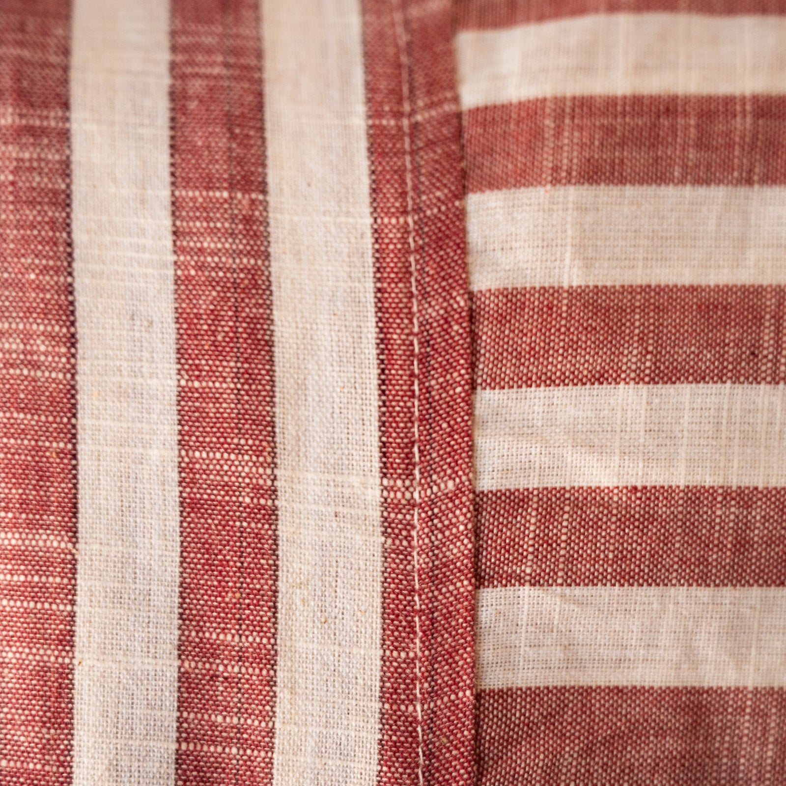Close-up of a woven textile with alternating vertical red stripes and horizontal off-white stripes, showing the fabric texture and stitching.