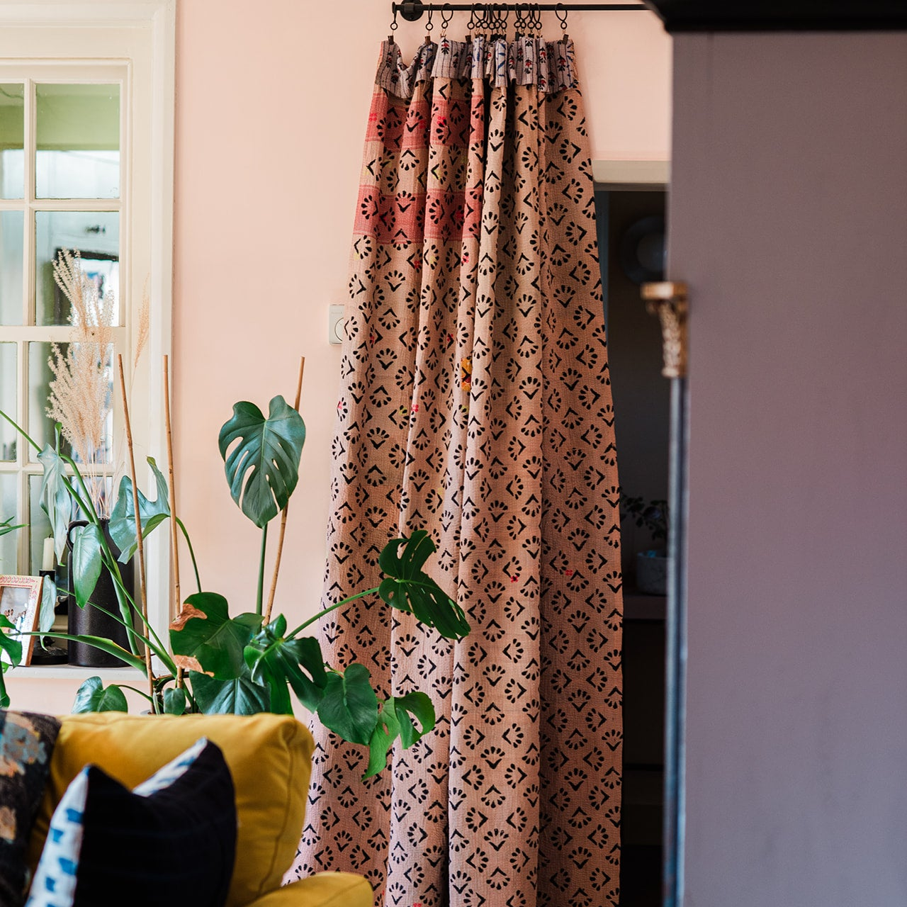 Patterned curtain hanging in a room with plants and furniture. 
Vintage-kantha-blanket-curtain-textiles-throw