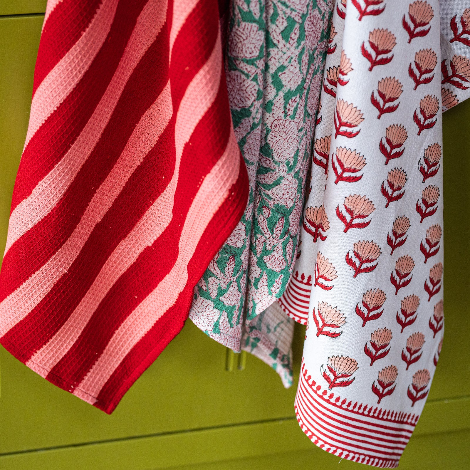 Three patterned towels hanging against a green background