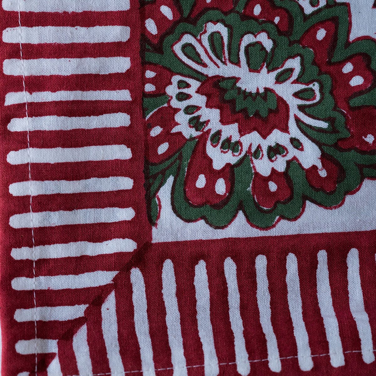 A close-up of a block-printed textile showing a red and green floral motif on a white base, alongside red and white striped sections.