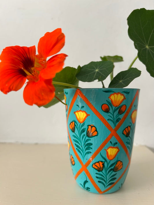 Decorative vase with floral patterns next to a red flower on a white background