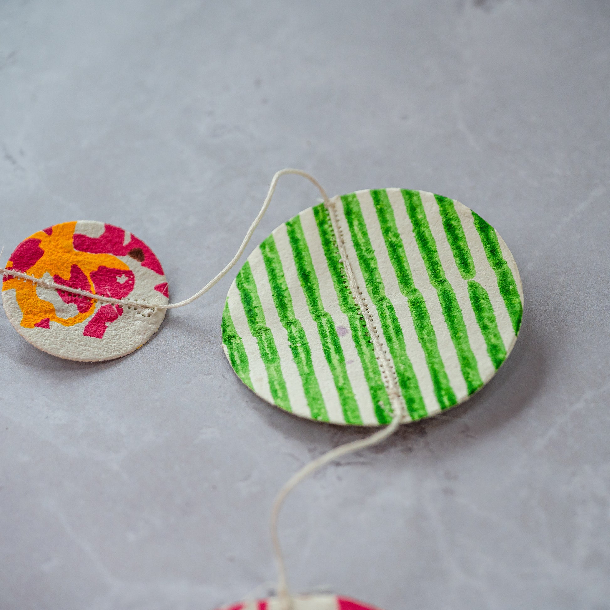 Decorative circular objects with green and white stripes and a pink floral design on a gray background