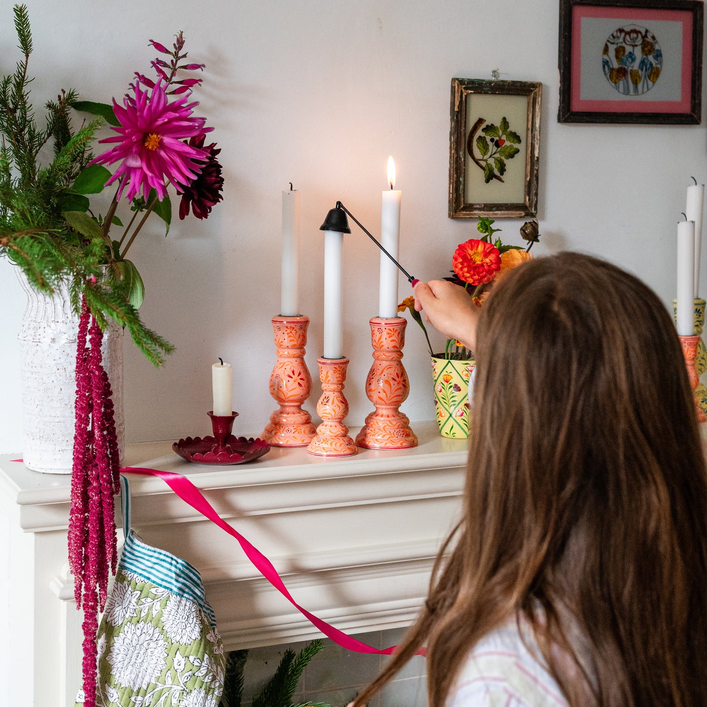 Person lighting candles on a decorative shelf with flowers and a framed picture in the background.