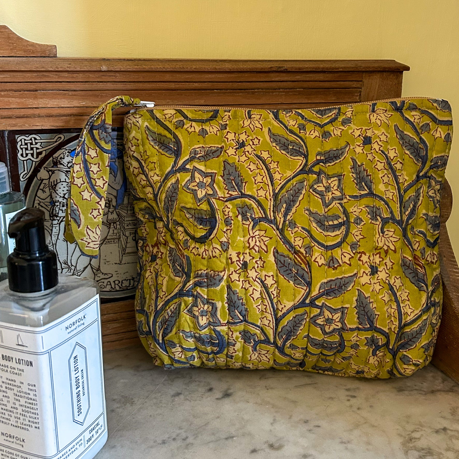 Floral-patterned cosmetic pouch on a wooden surface with a bottle of lotion in the foreground. cosmetic pouch block printed