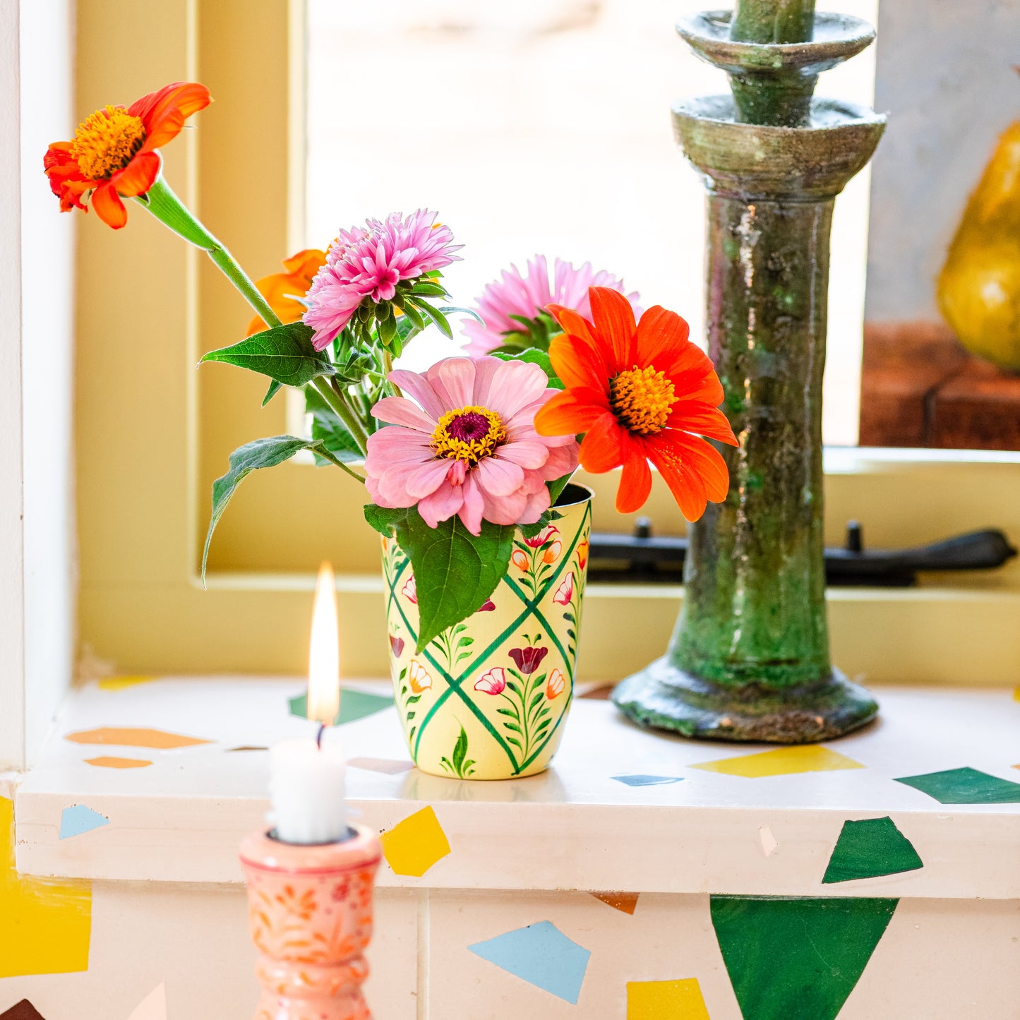 Decorative table with flowers in a vase, candles, and colorful geometric patterns. hand painted vase floral cream. Vase cream hand painted