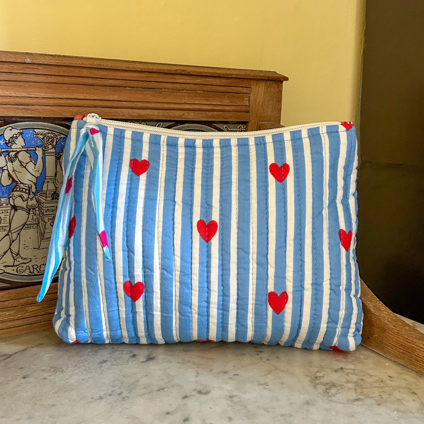 Blue and white striped pouch with red hearts on a marble surface. love hearts flat pouch
