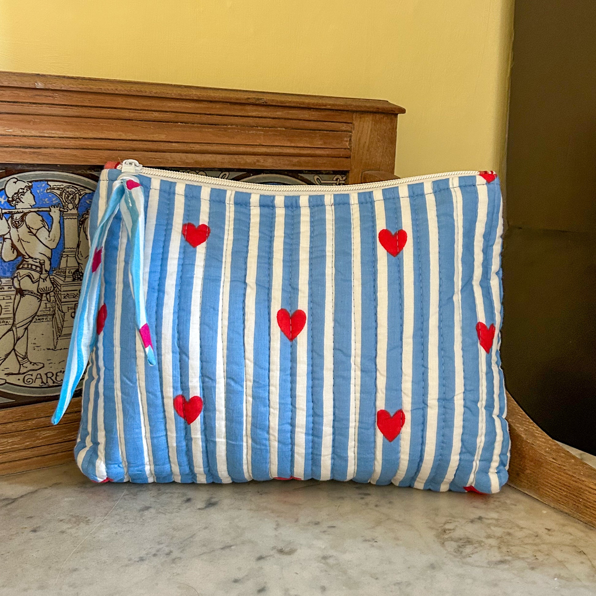 Blue and white striped pouch with red hearts on a marble surface. love hearts flat pouch