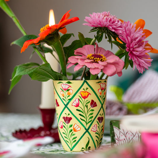 Decorative flowerpot with flowers and a lit candle on a table. hand painted vase floral cream