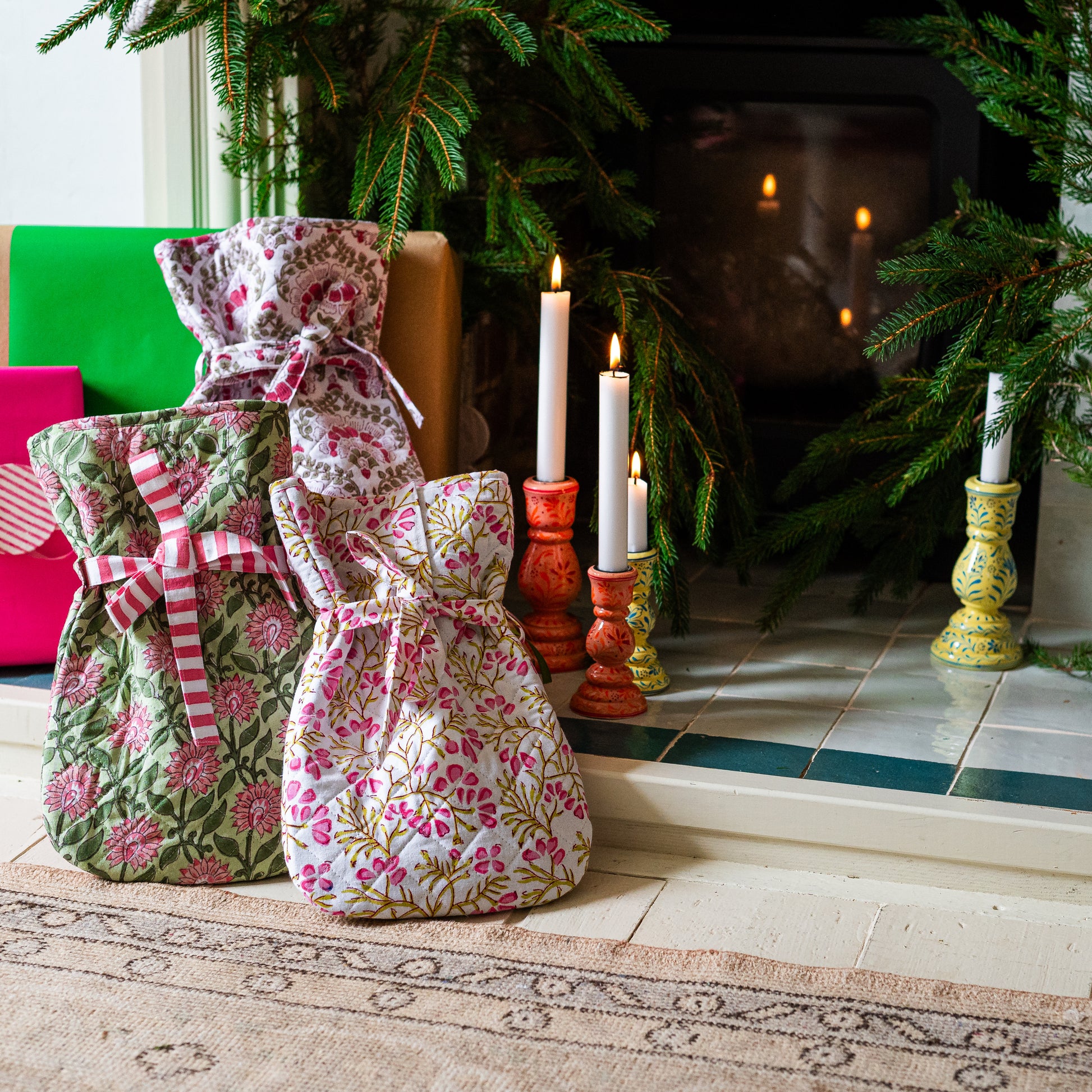Floral hot water bottles  on a rug with candles and a fireplace in the background