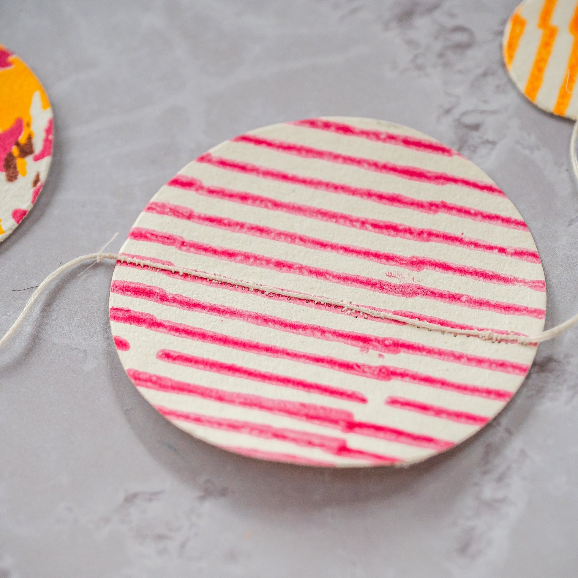 Round wooden coaster with pink and white striped pattern on a gray surface