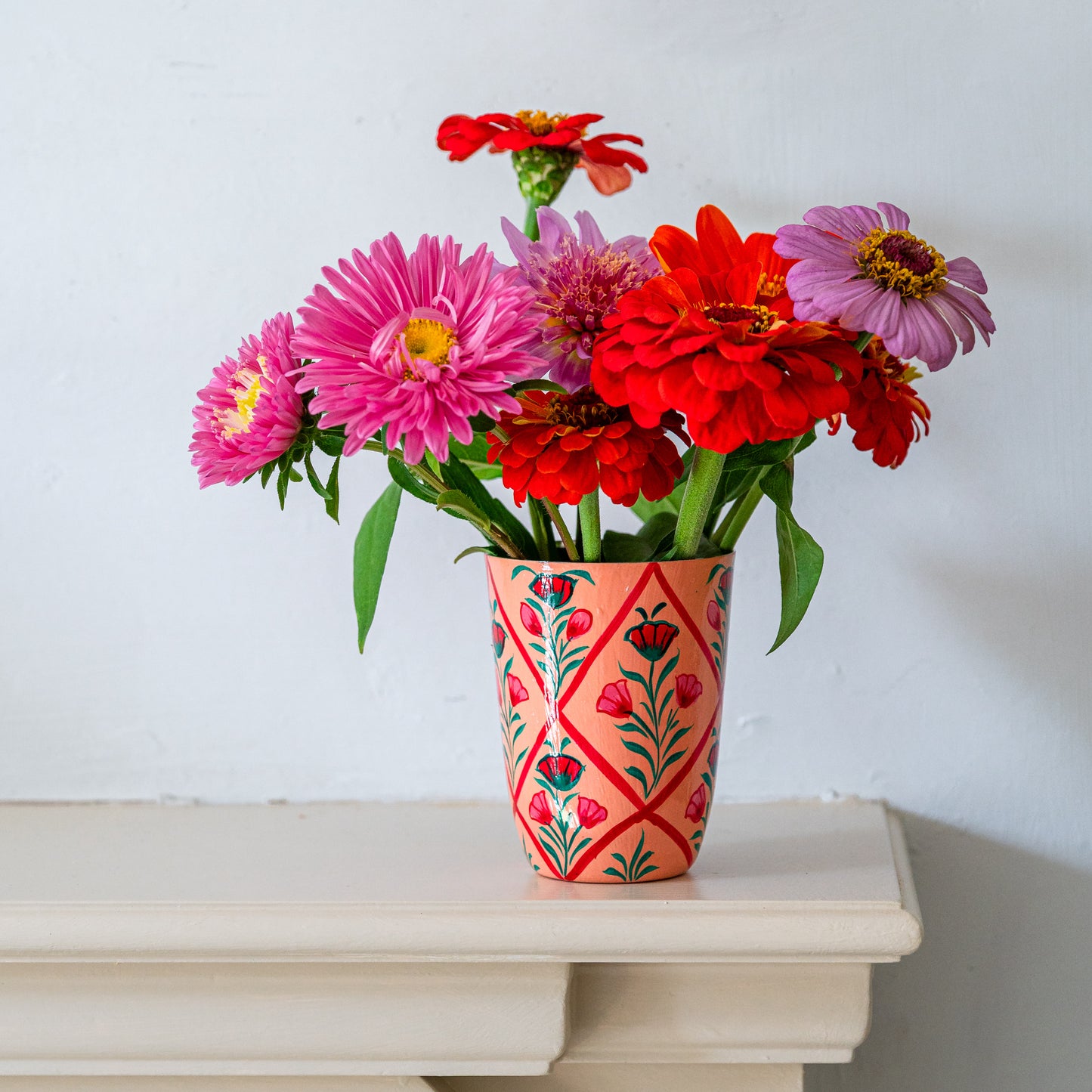 Colorful flowers in a hand-painted vase on a white surface with a light gray background. constance and denny floral