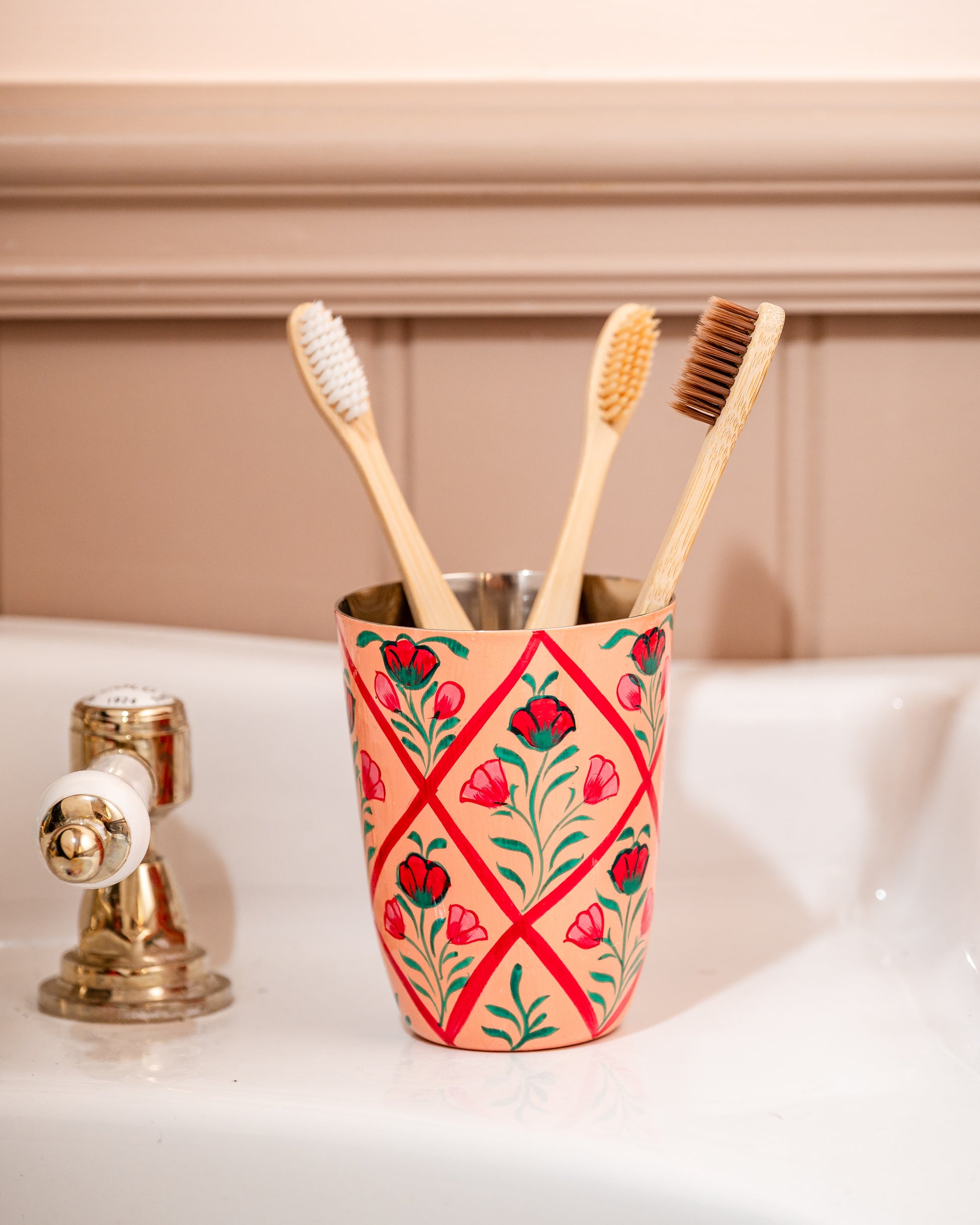 Decorative toothbrush holder with floral design holding wooden toothbrushes on a bathroom sink.