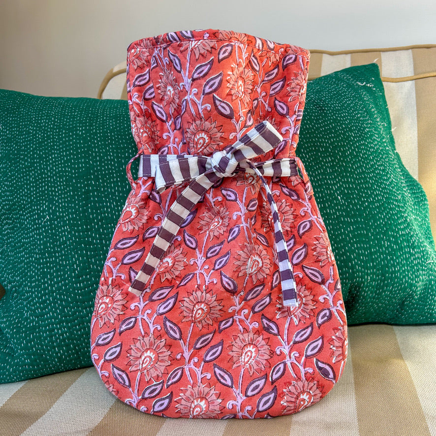 Red floral-patterned hot water bottle with a striped ribbon on a green cushioned surface.