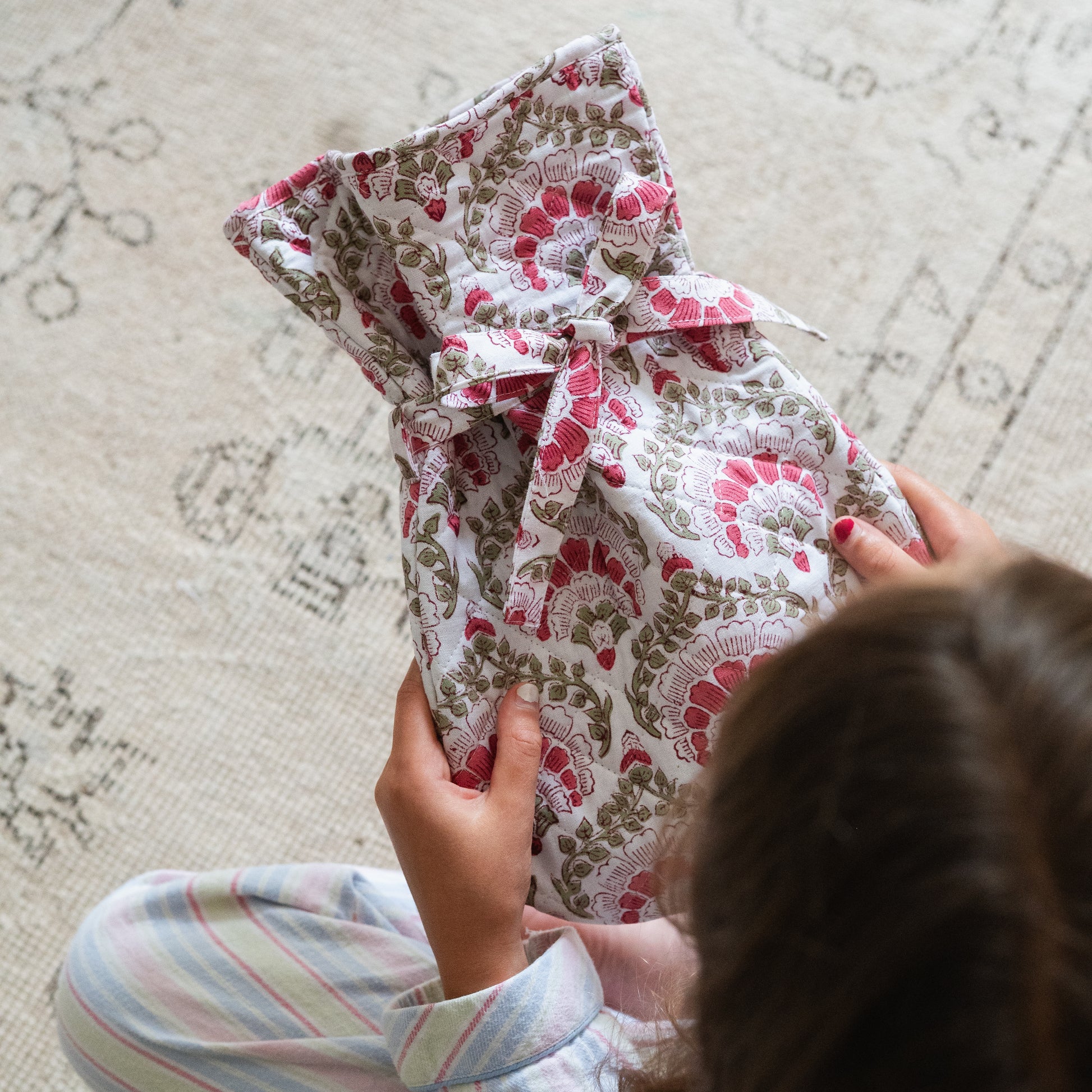 Person holding a hot water bottle with floral pattern on a textured surface