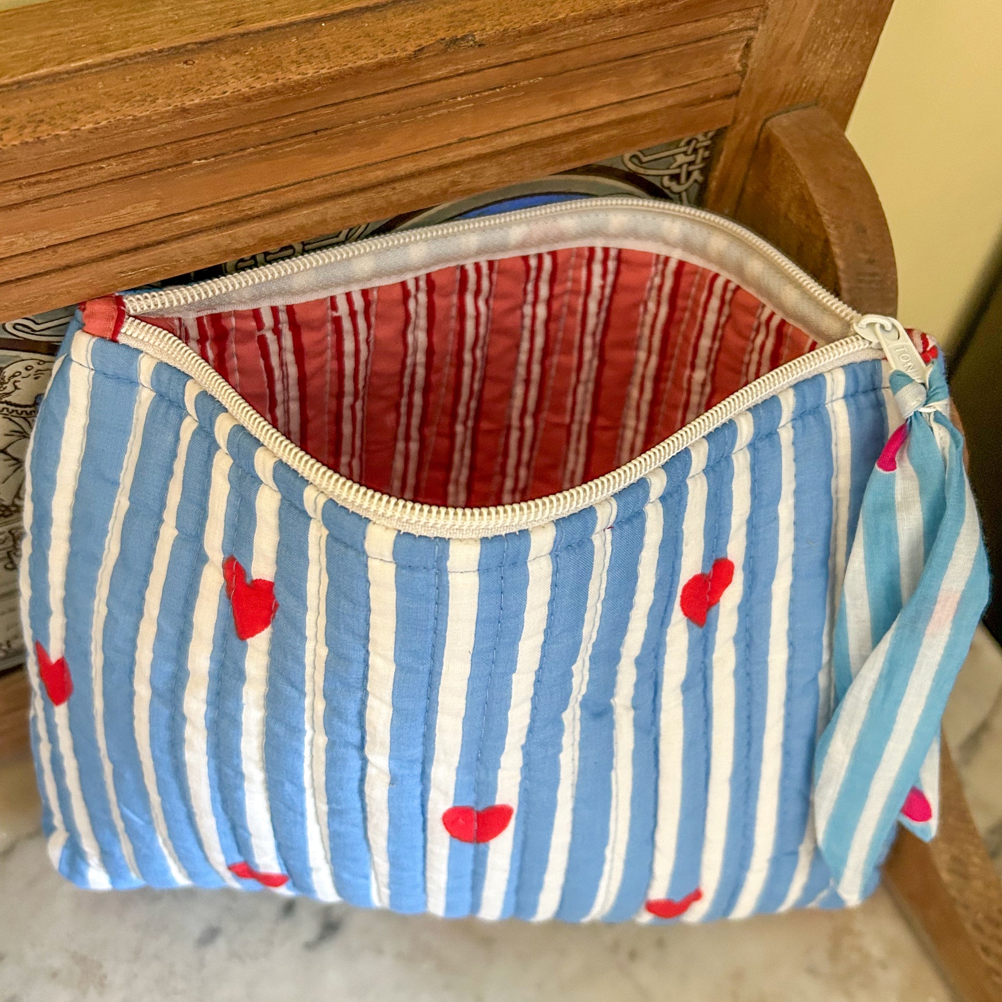 Fabric pouch with blue and white striped pattern and red hearts on a wooden surface.