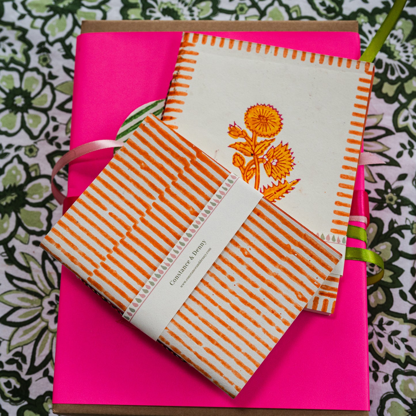 Notebook with orange floral design and striped cover on a pink background