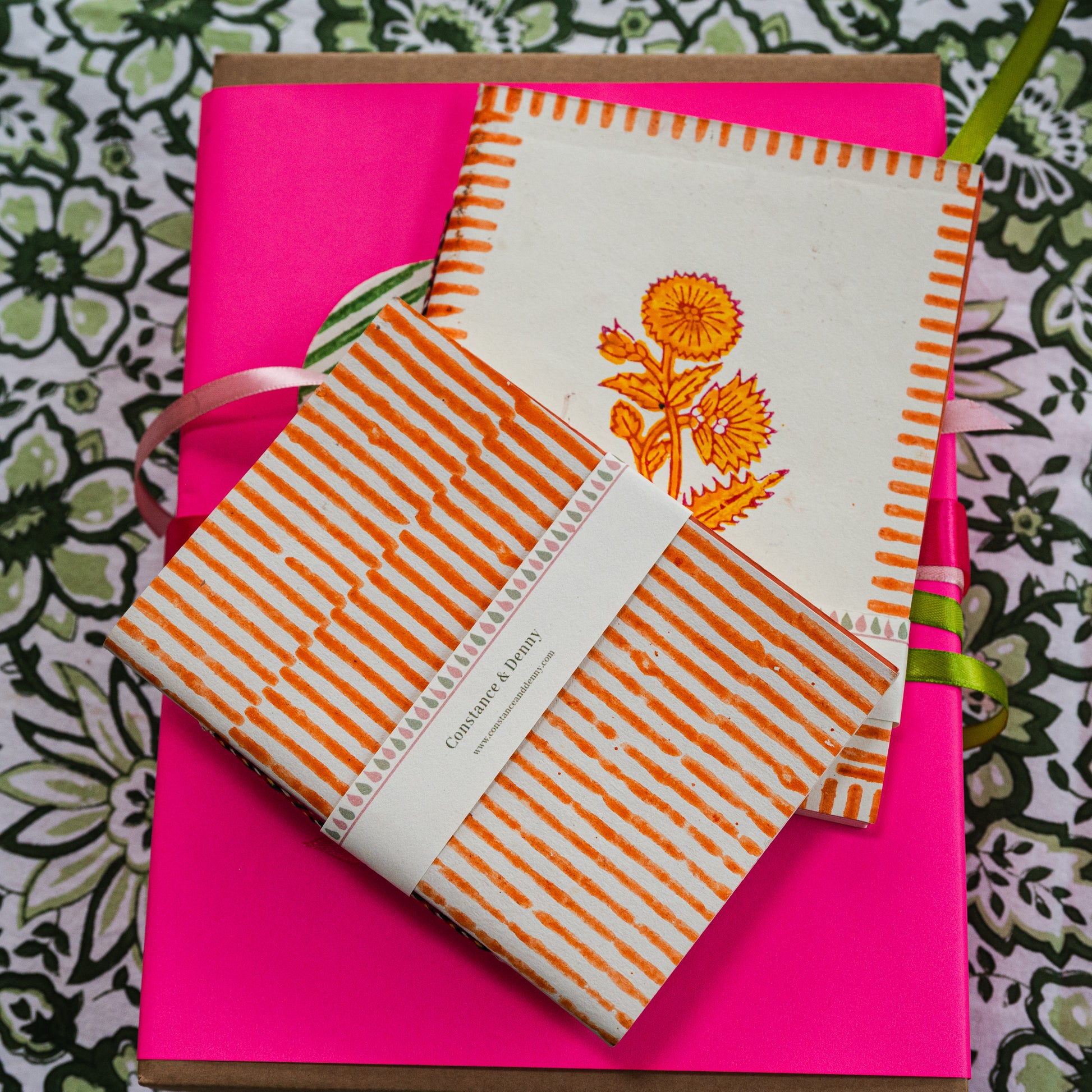 Notebook with orange floral design and striped cover on a pink background