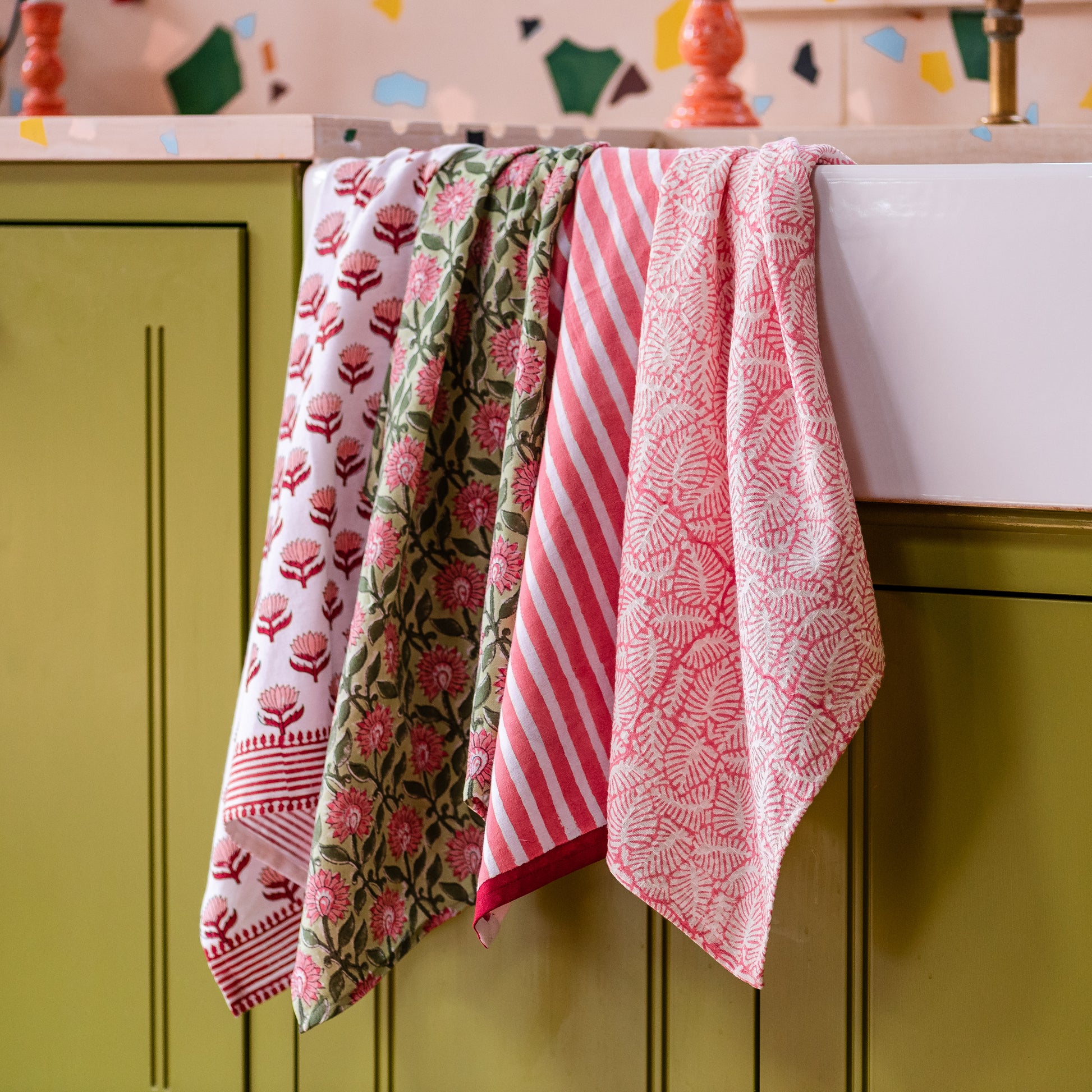 Colorful kitchen tea towels hanging on a green cabinet with a patterned backsplash.