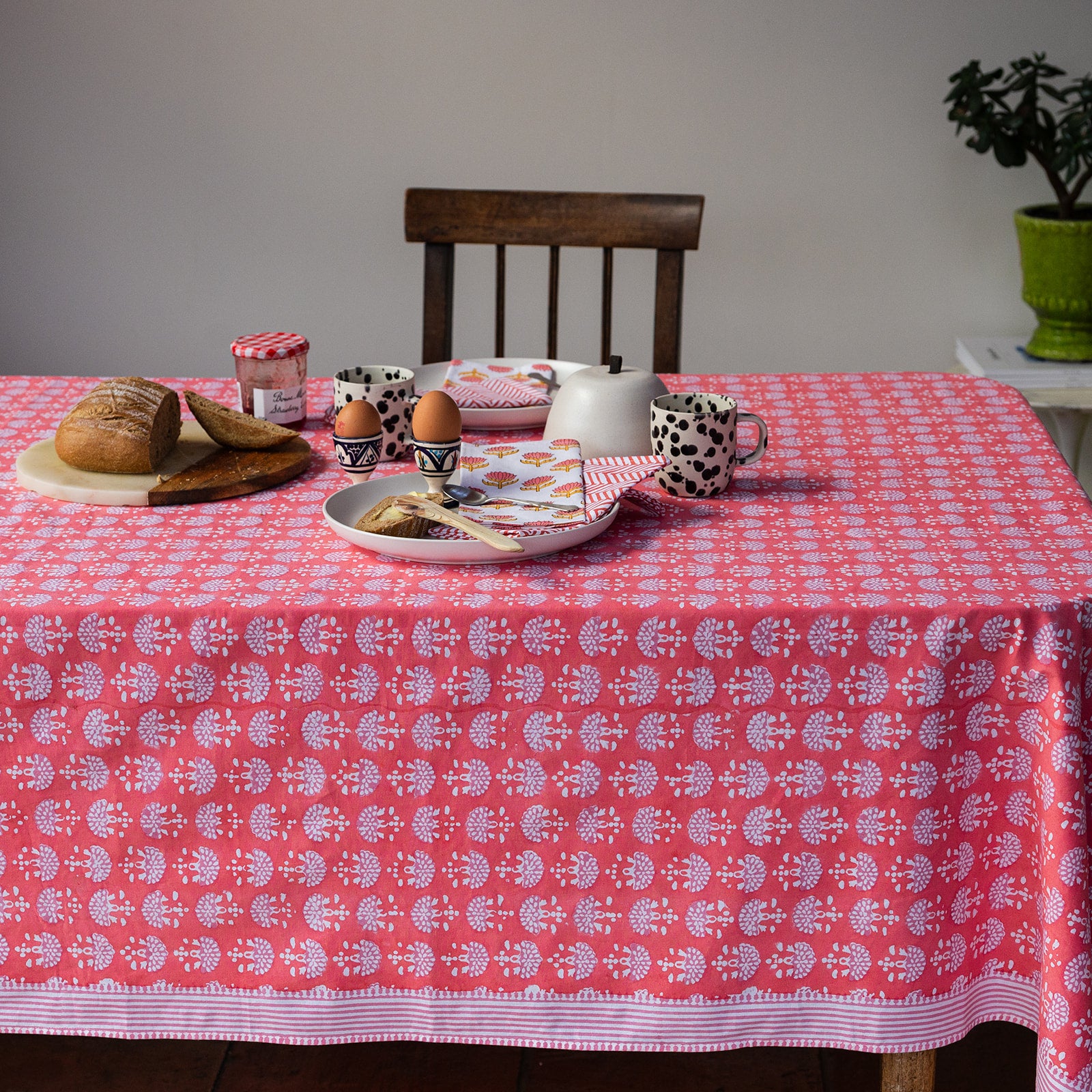 Table with a pink patterned tablecloth, food items, and a chair.