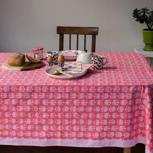 Table with a pink patterned tablecloth, food items, and a chair.