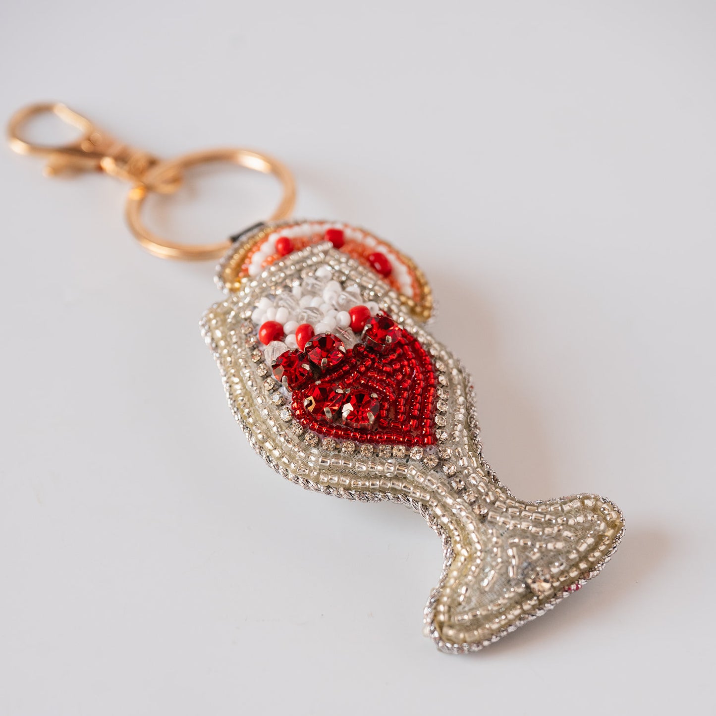 A cocktail keychain charm embellished with red and white beads, featuring a gold-tone clasp and split ring, photographed on a light gray background.