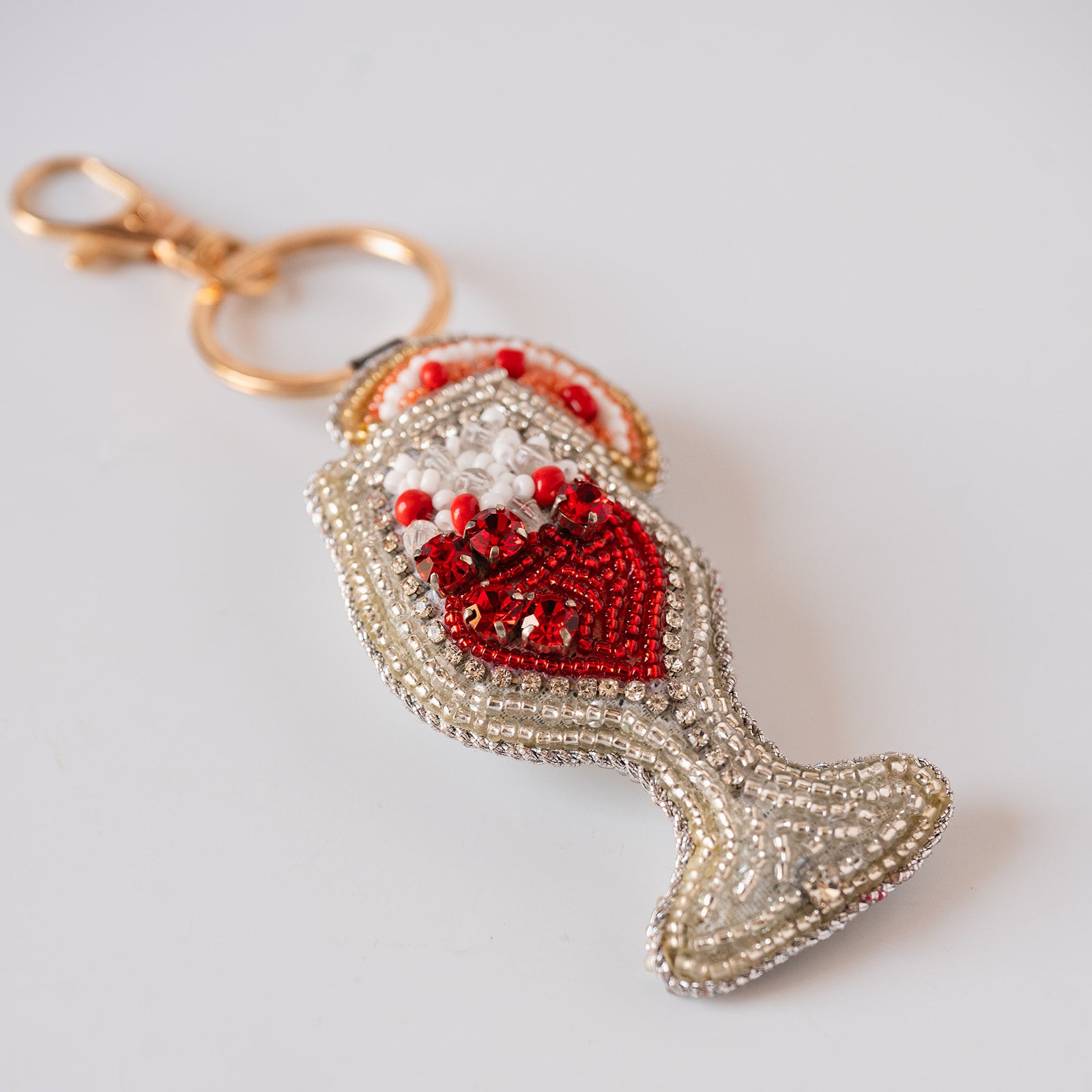 A cocktail keychain charm embellished with red and white beads, featuring a gold-tone clasp and split ring, photographed on a light gray background.