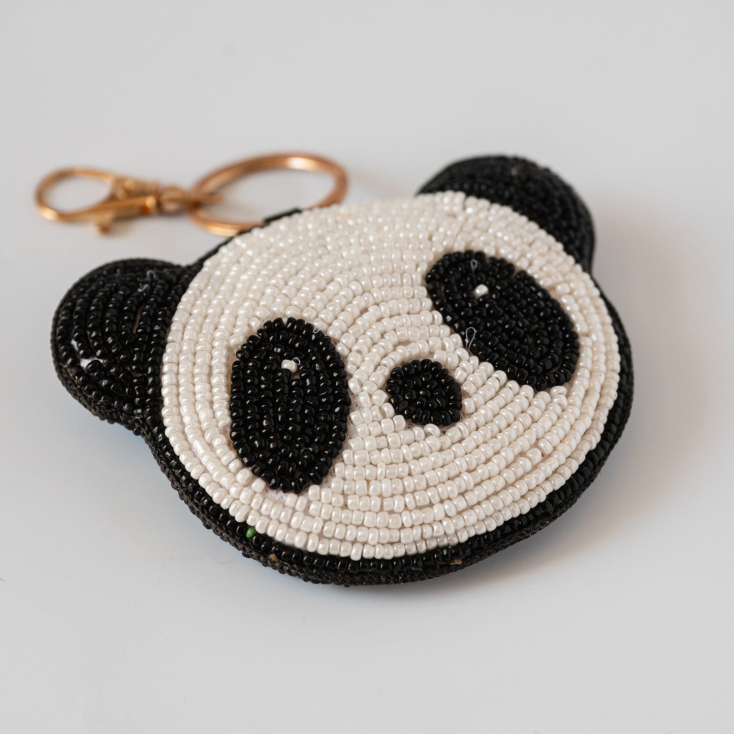 A beaded panda shaped keychain charm with a gold clasp, featuring black and white beads to make a panda face.