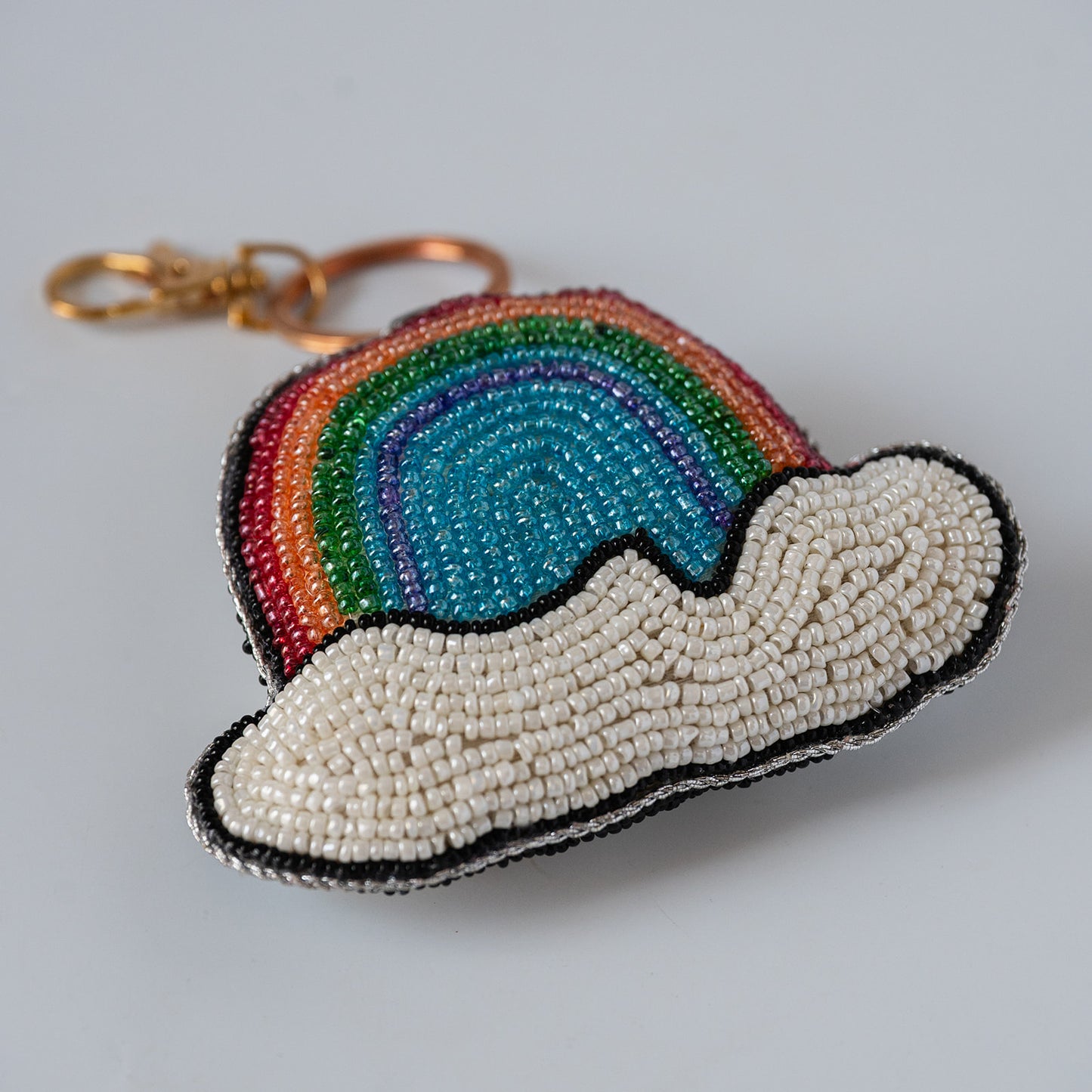 A beaded rainbow and cloud shaped keychain charm with a gold clasp, featuring multi coloured beads to make a a rainbow sitting on a cloud.