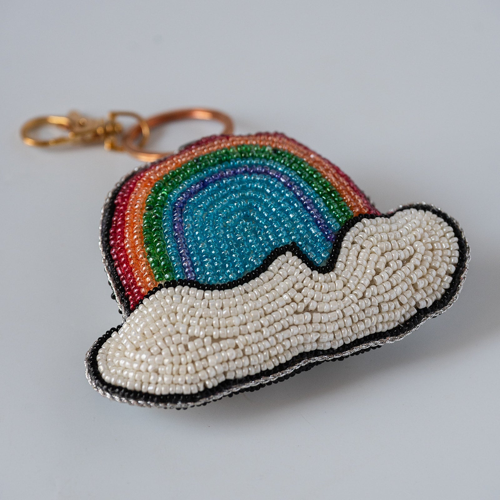 A beaded rainbow and cloud shaped keychain charm with a gold clasp, featuring multi coloured beads to make a a rainbow sitting on a cloud.