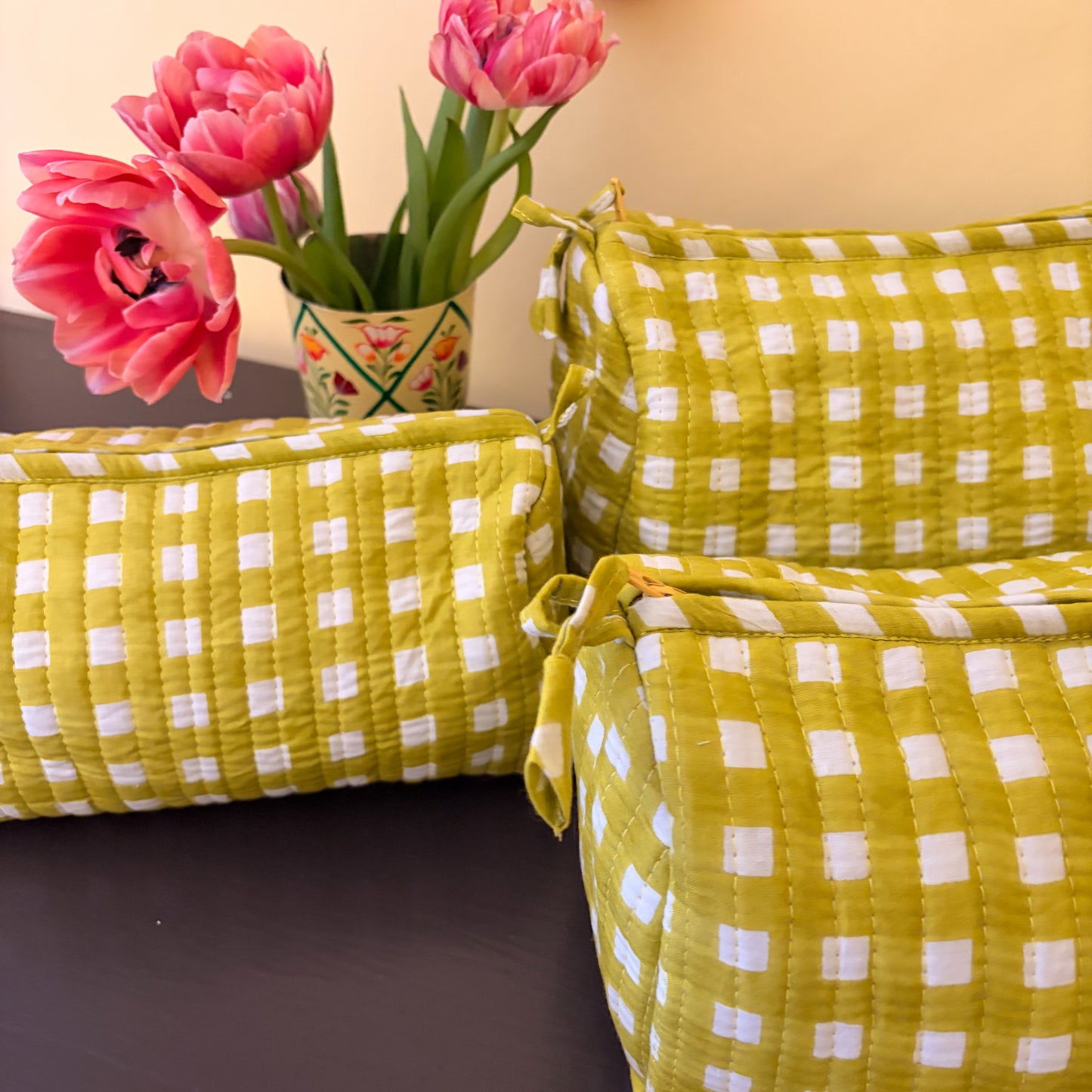 alchemilla and white checkered cushions with pink tulips in a vase on a dark surface.