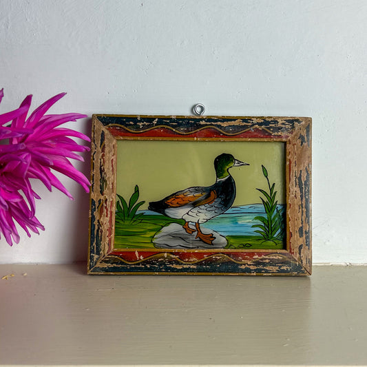 Decorative painting of a duck in a wooden frame on a shelf with a pink flower.