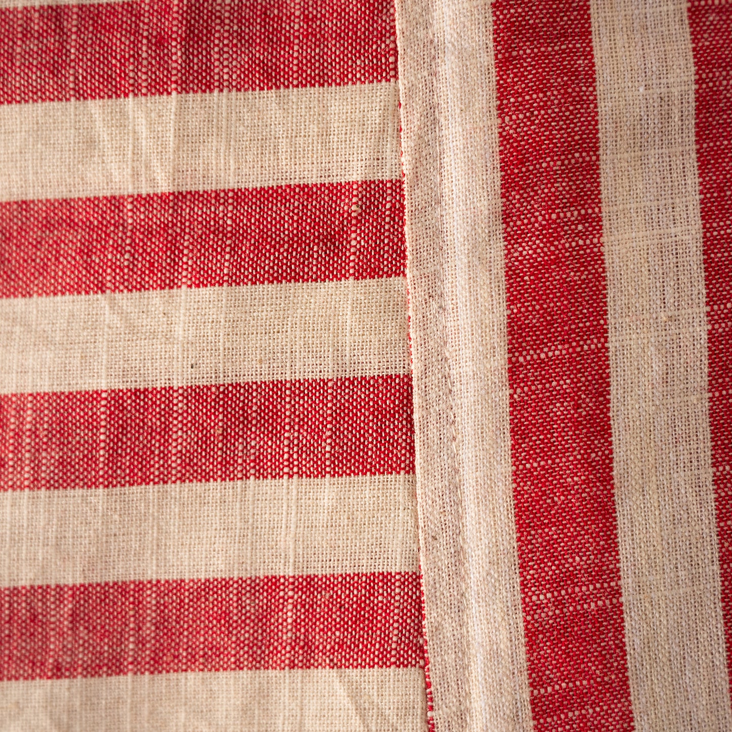 A close-up of a woven textile with alternating red and warm off-white horizontal stripes and a vertical off-white border.