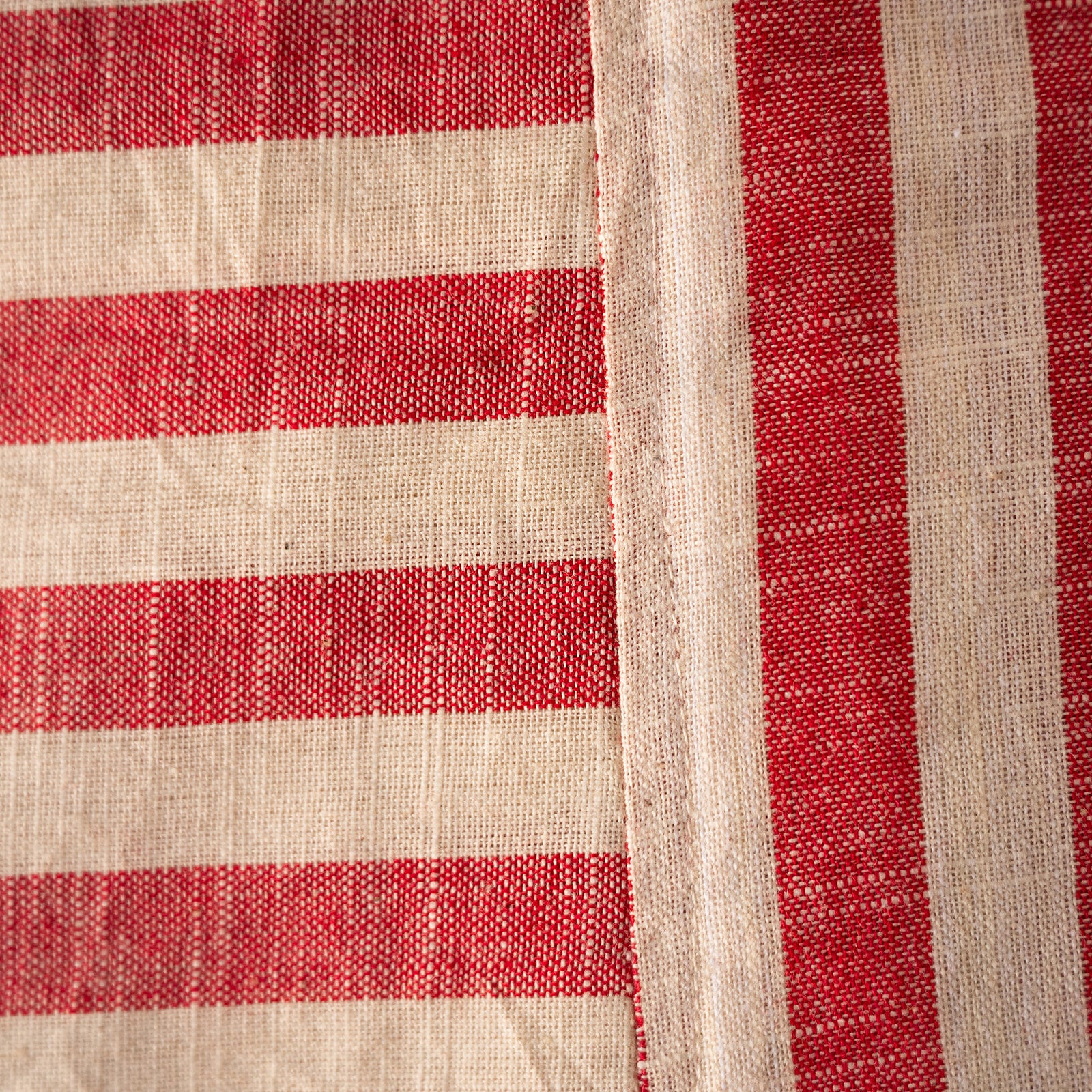 A close-up of a woven textile with alternating red and warm off-white horizontal stripes and a vertical off-white border.