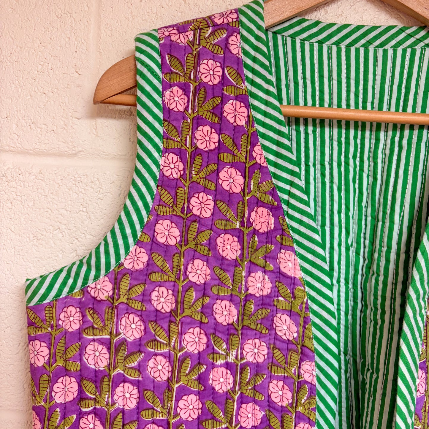 waistocoat with floral and striped patterns hanging on a wooden rod against a light background.