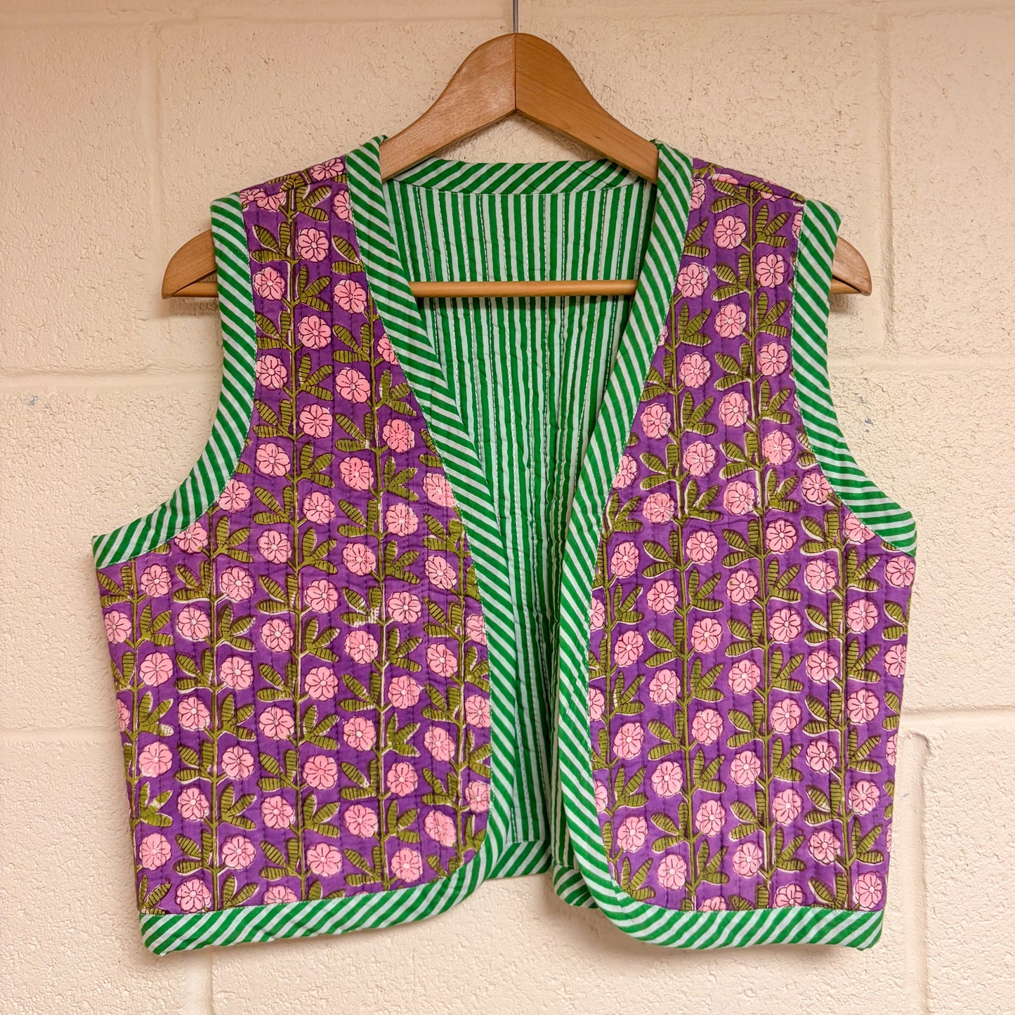 Vest with purple floral and green striped pattern on a hanger against a beige wall.