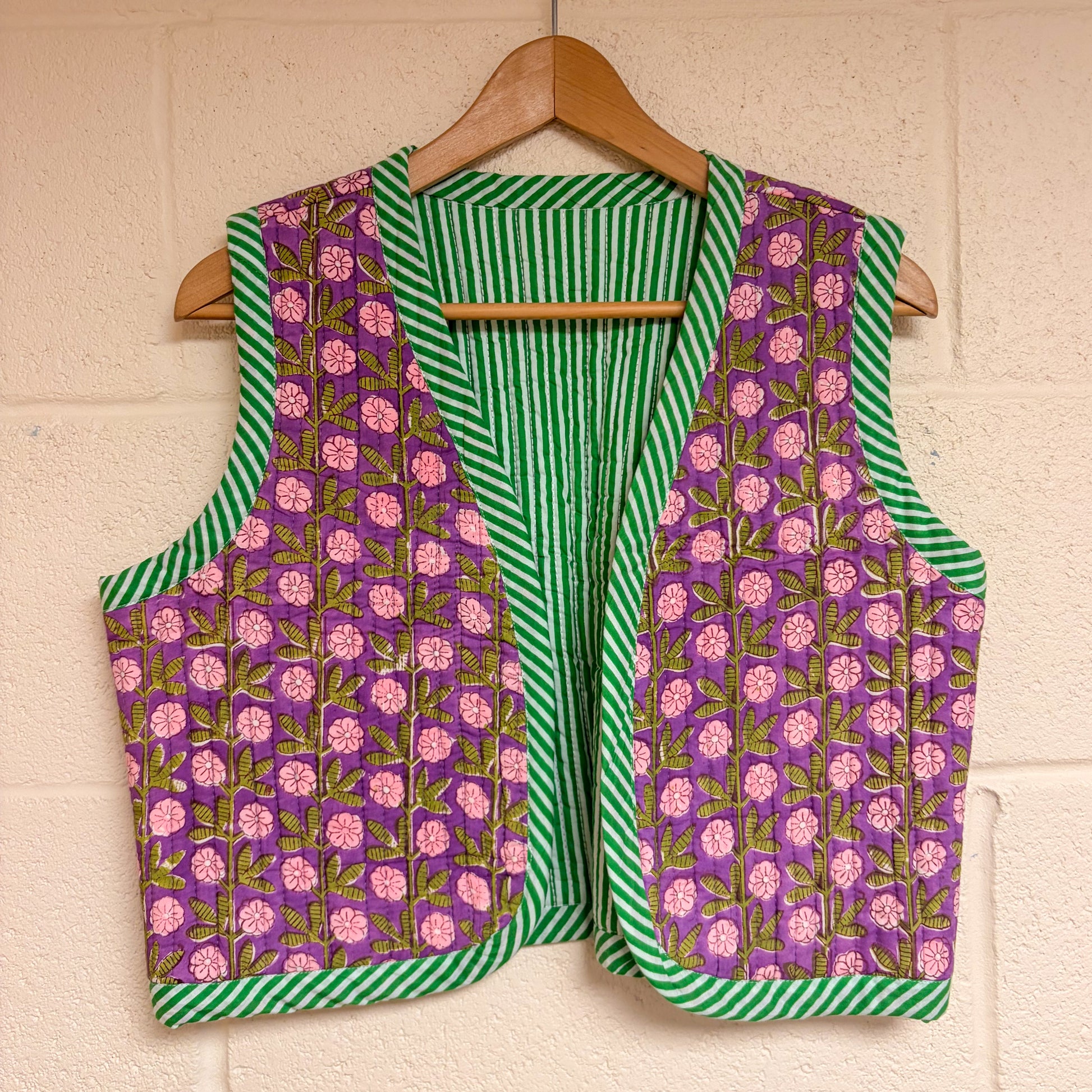 Vest with purple floral and green striped pattern on a hanger against a beige wall.
