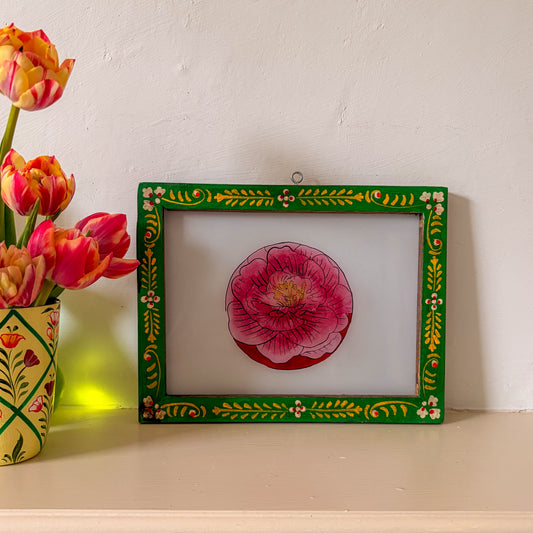 Decorative framed artwork of a pink flower on a white surface with tulips in the background.