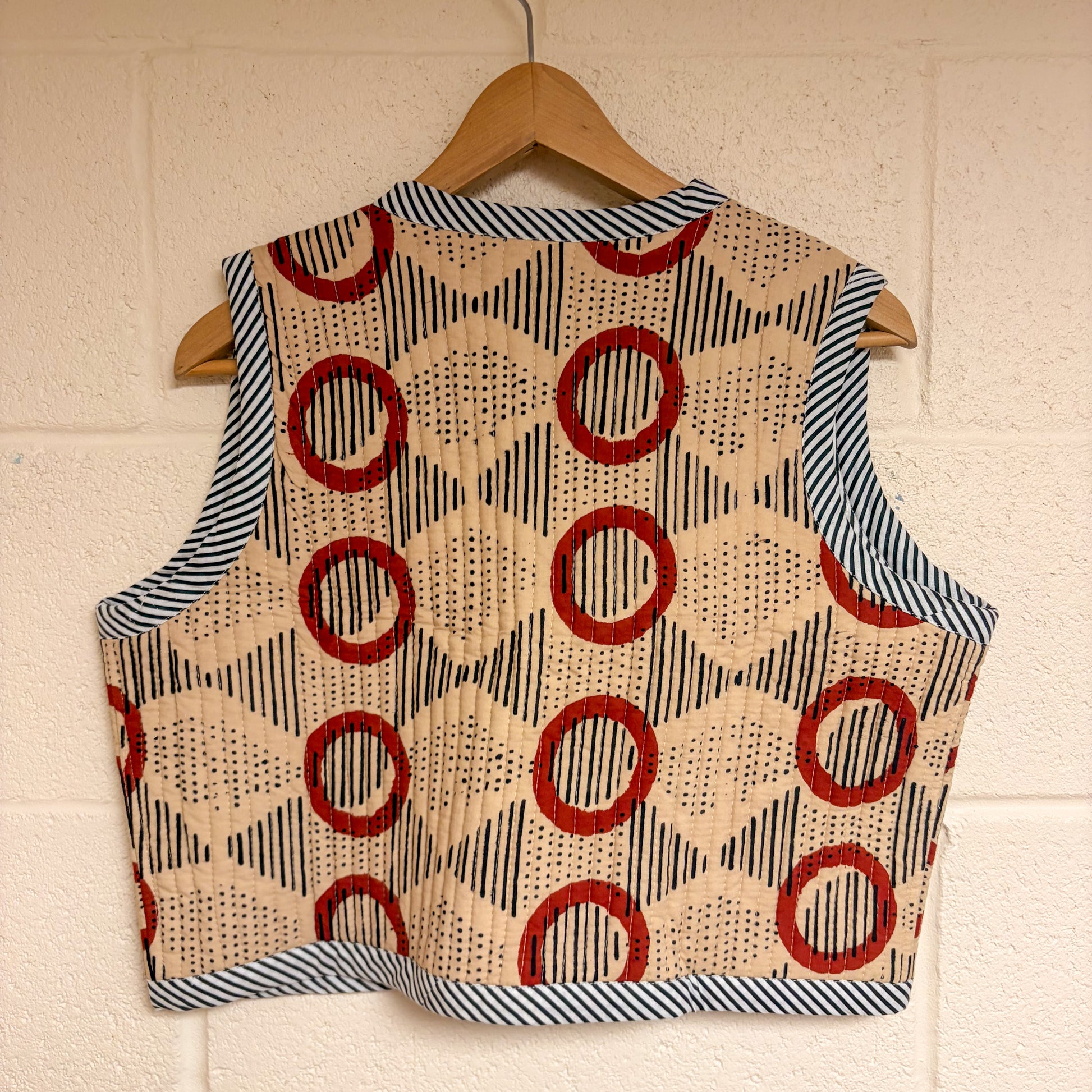 Vest with geometric pattern on a hanger against a white brick wall.