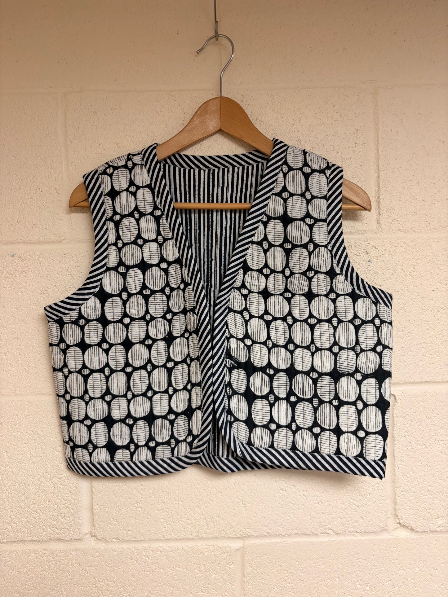 Black and white patterned vest on a hanger against a beige wall.